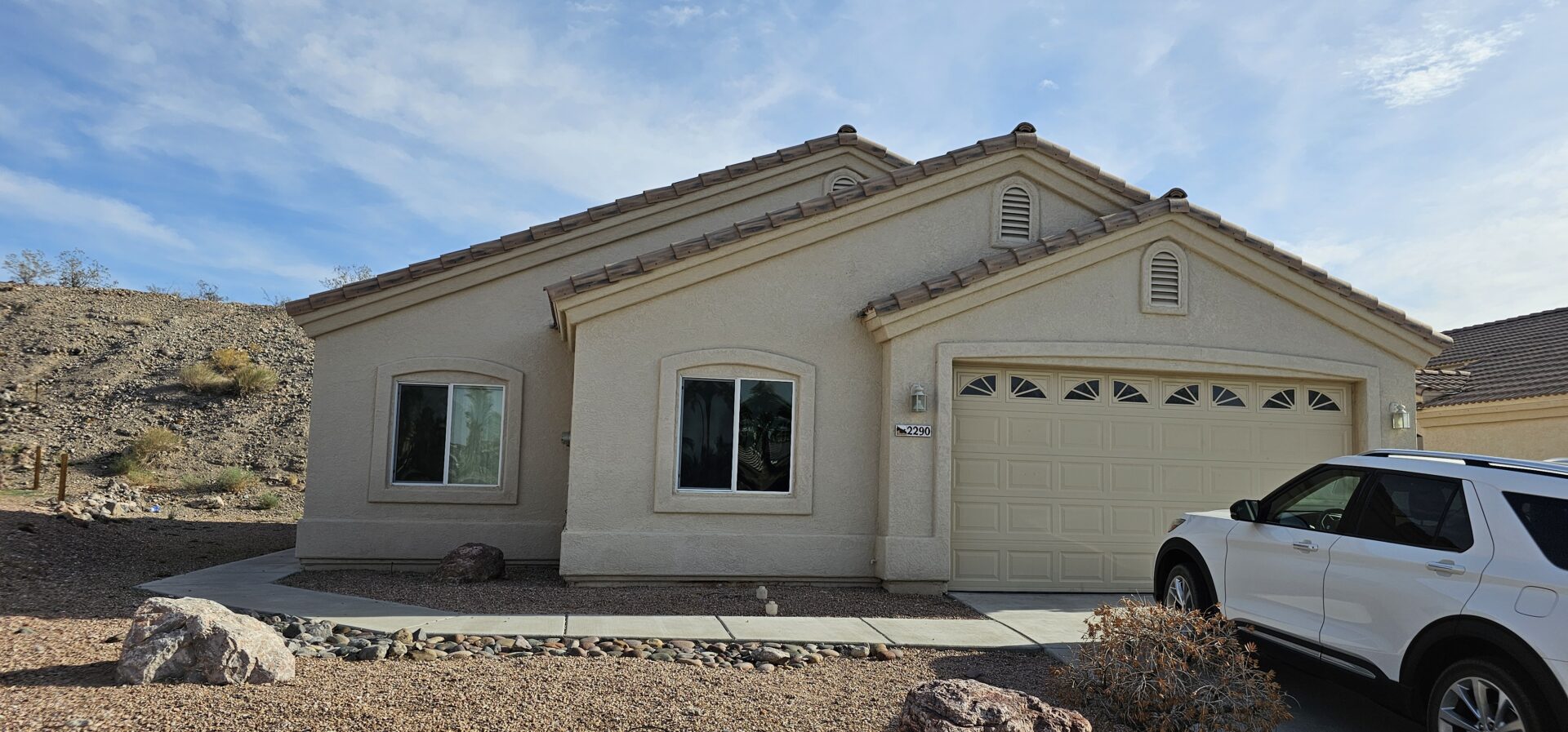 Tan house with white SUV in driveway.