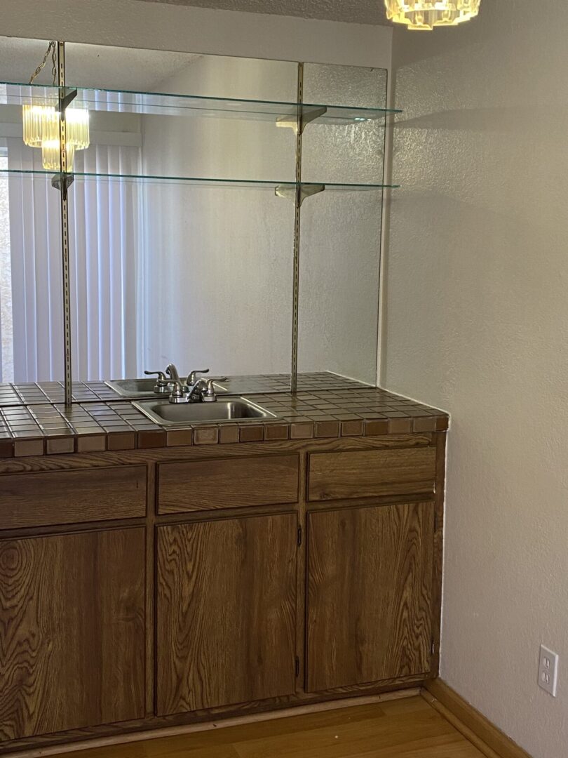 Wood cabinets, tiled counter, sink, glass shelves