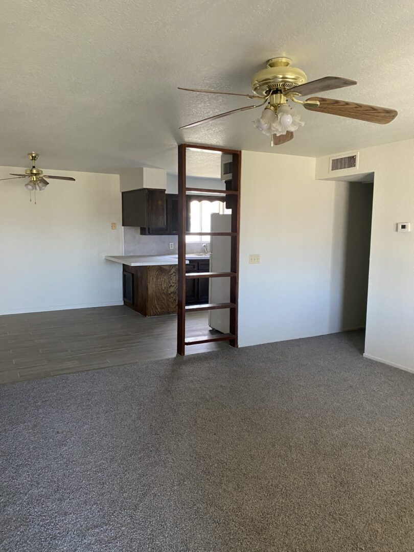 Carpeted living room with ceiling fans and kitchen